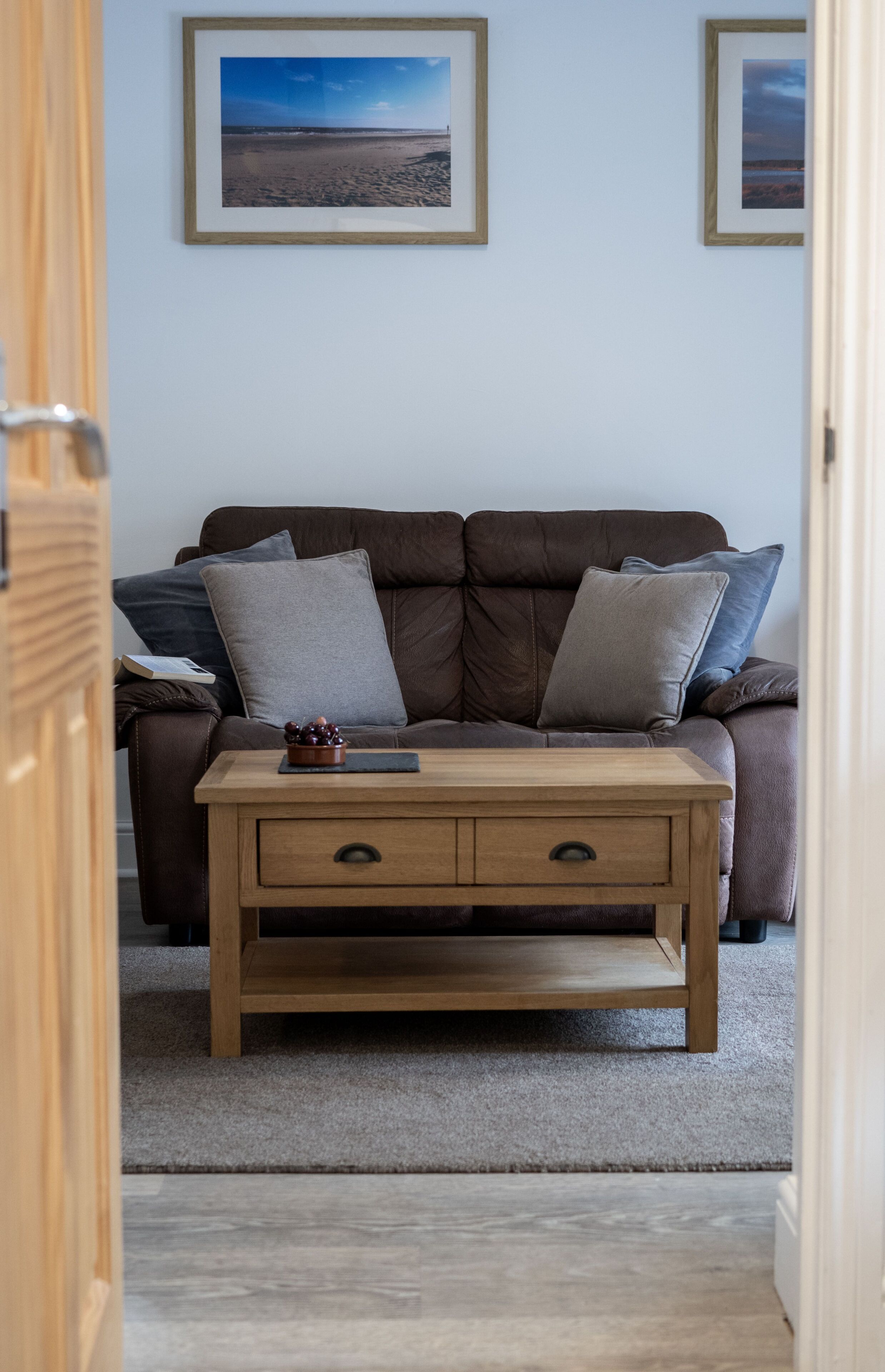 A room with a brown leather sofa, a wooden side table with a drawer, and two framed pictures on the wall.