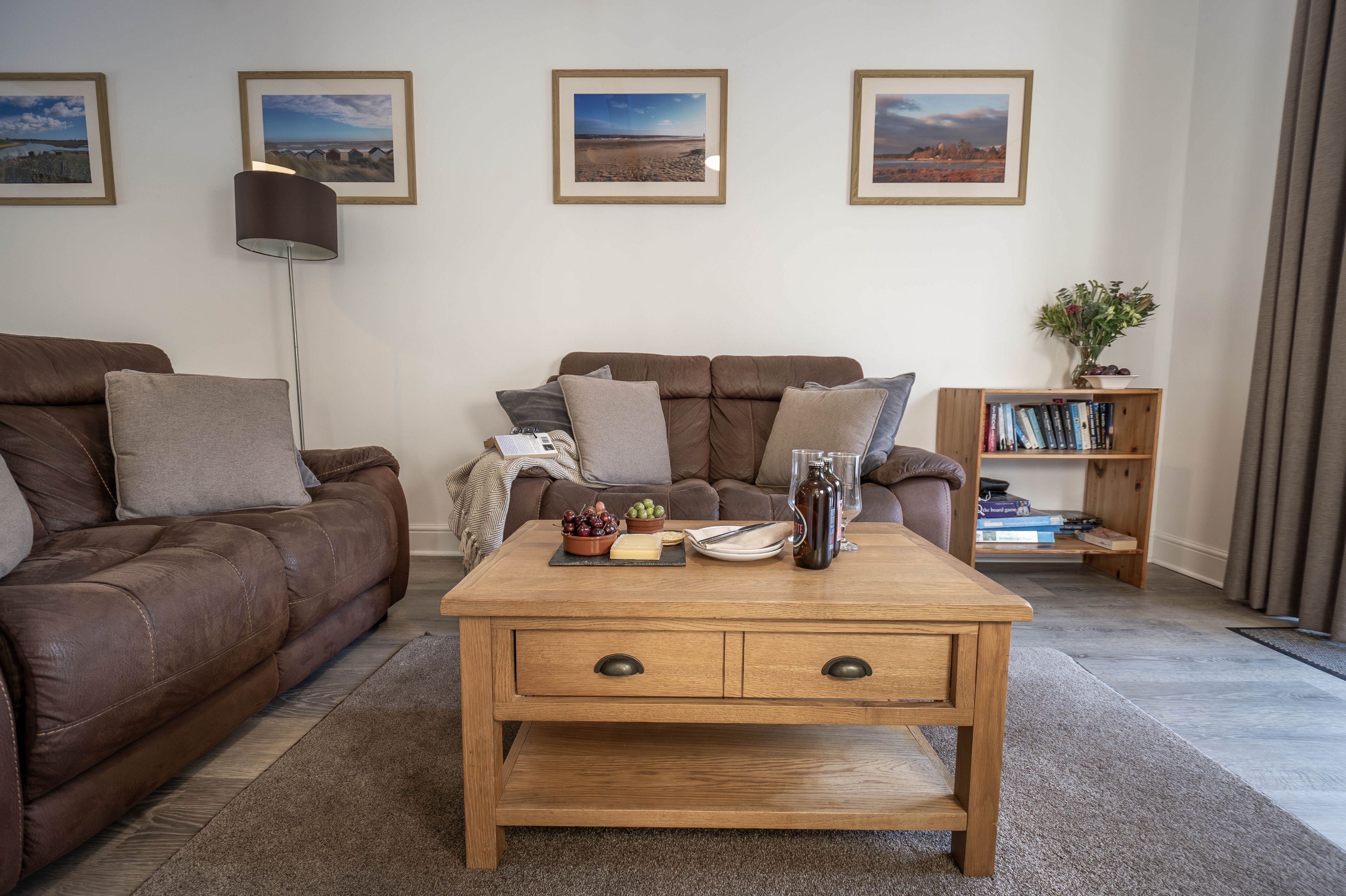 A living room with a brown leather sofa, a wooden coffee table with a bowl of grapes and a bottle, and a bookshelf with books.