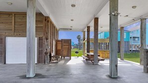 Un'area esterna riparata con panche e tavoli in legno, un pavimento in cemento e vista su edifici colorati sullo sfondo.