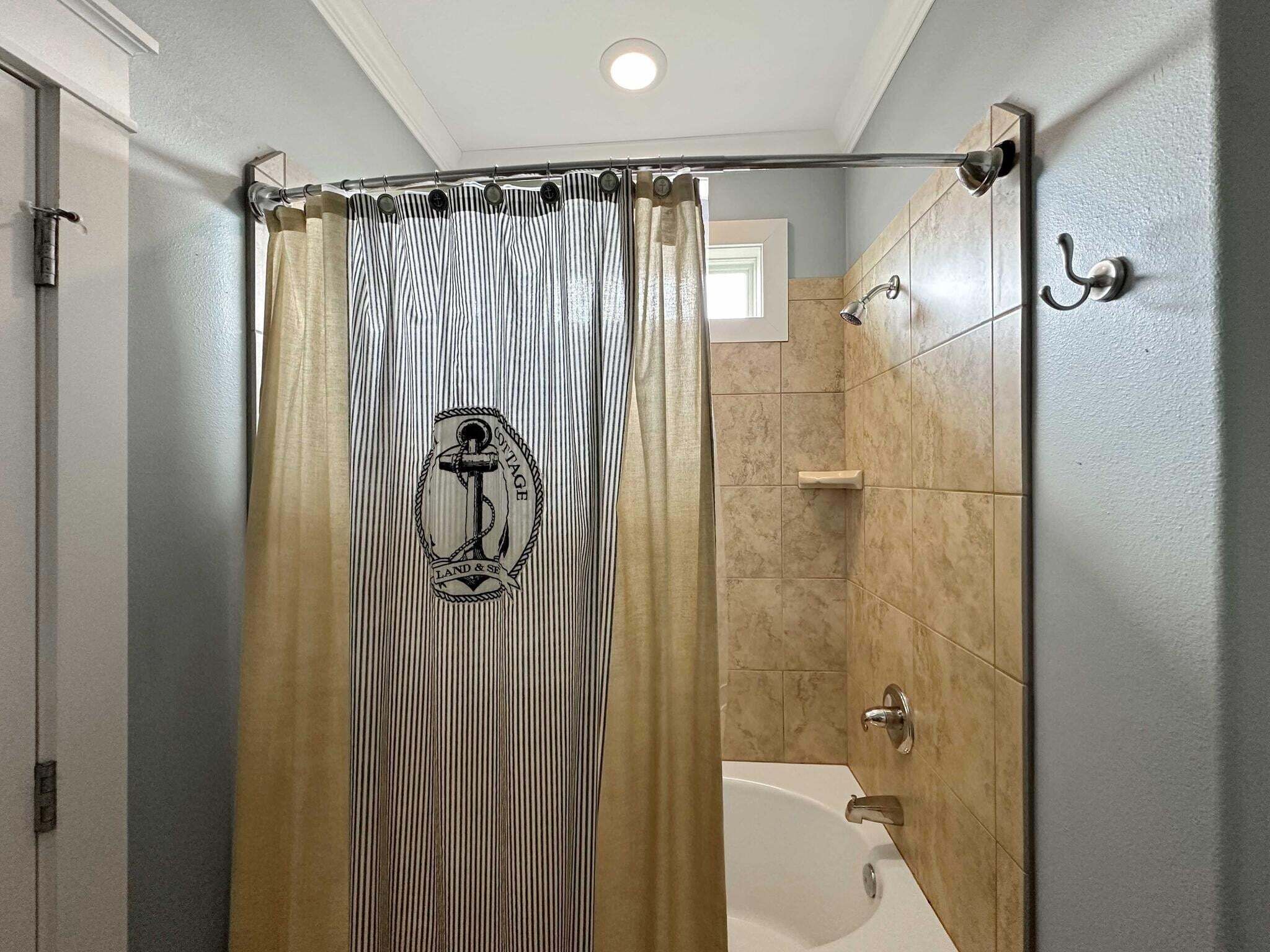 A bathroom with a shower curtain featuring a nautical design, a bathtub, and tiled walls.