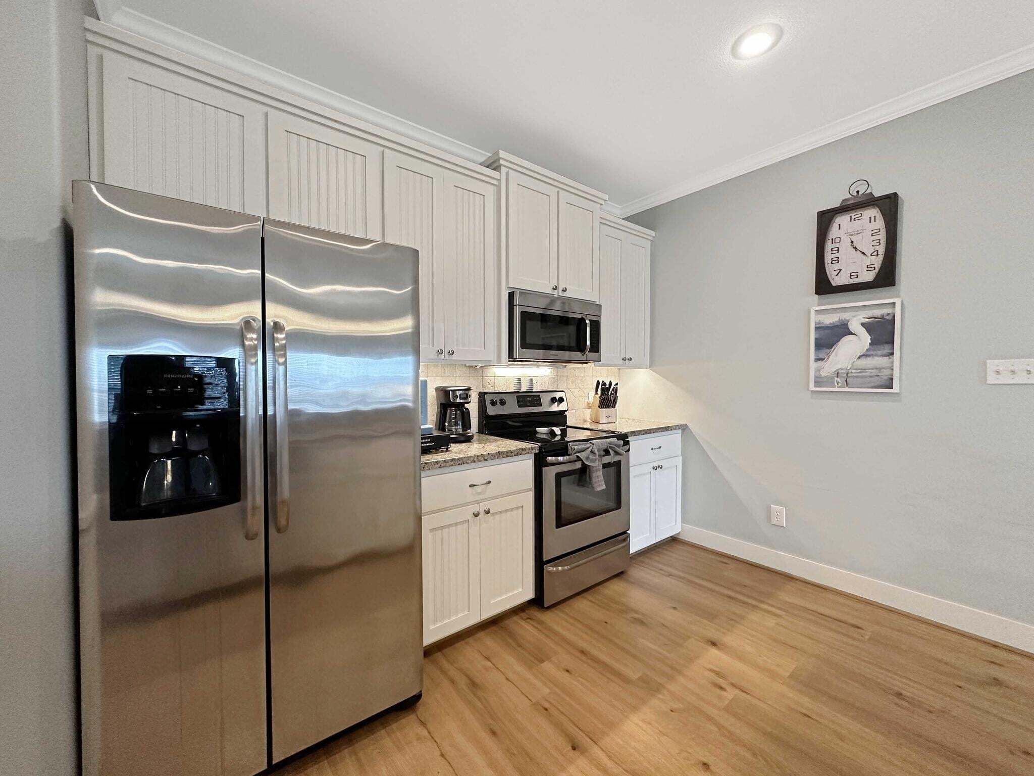 A kitchen with white cabinets, stainless steel appliances, a microwave, a coffee maker, and a clock on the wall.
