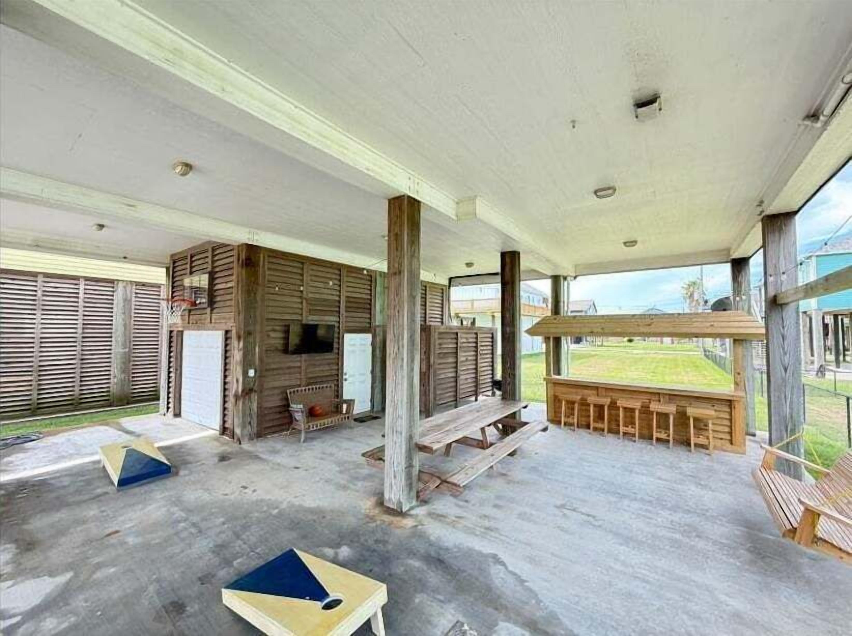 A covered outdoor area with wooden benches, a basketball hoop, and a view of the outdoors.