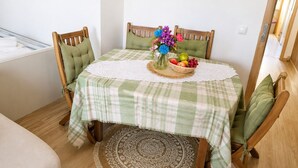 En matplats med ett bord dukat för två personer, med en grön- och vitrutig duk, trästolar med gröna kuddar, en vävd bordsdekoration och en vas med blommor.