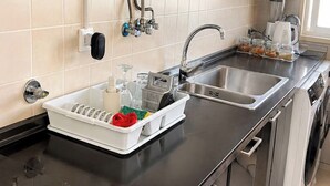 Ett kök med en diskho i rostfritt stål, ett diskställ, en kaffebryggare och en vattenkokare.