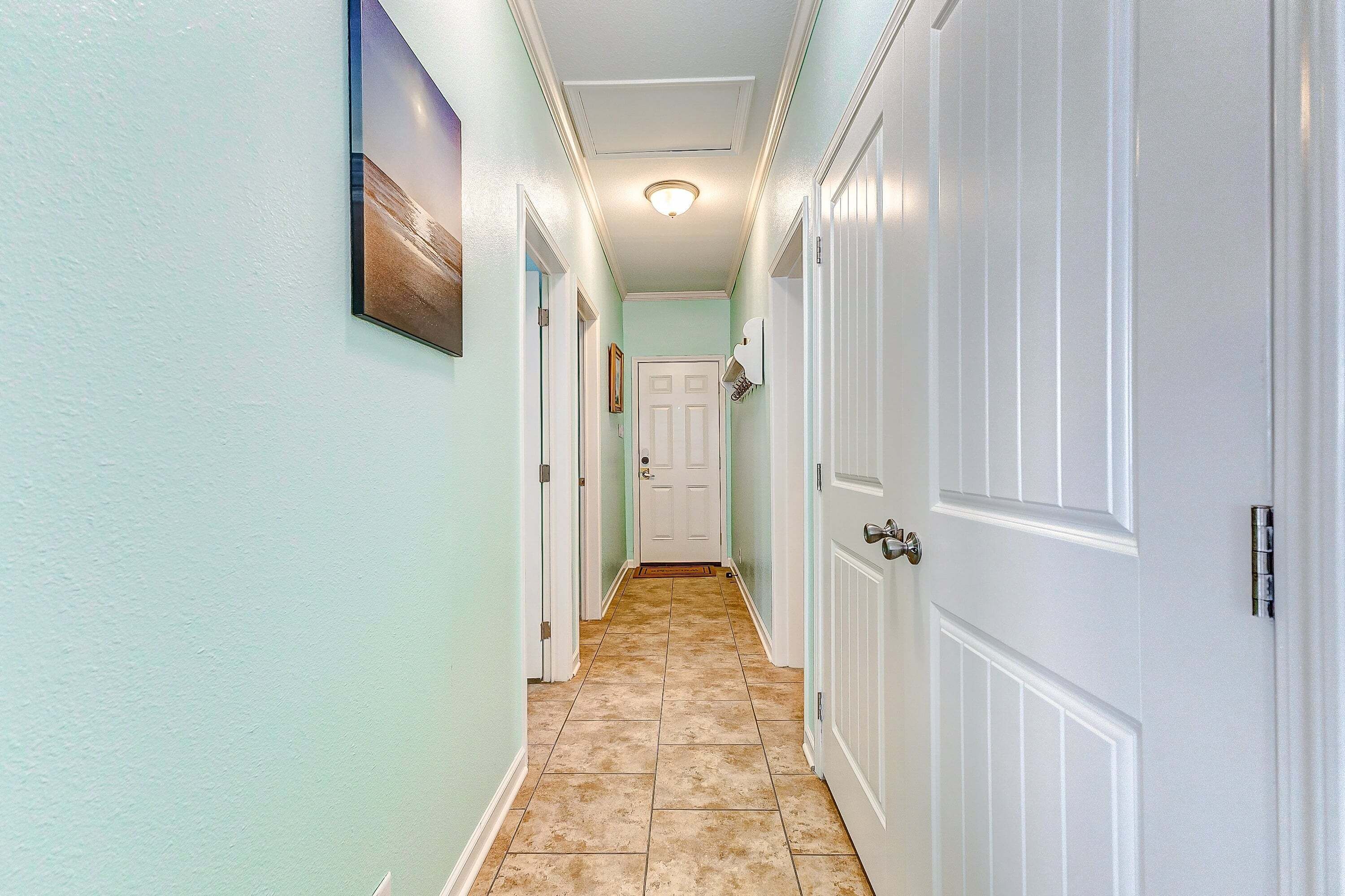 A hallway with light green walls, white doors, and a tiled floor.