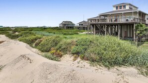 A coastal house with a wooden deck and a balcony, surrounded by vegetation and a sandy path. - A Stairway To Heaven 4 Bedroom Home (Port Bolivar)