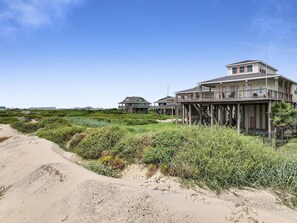 A coastal house with a wooden deck and a balcony, surrounded by vegetation and a sandy path. - A Stairway To Heaven 4 Bedroom Home (Port Bolivar)