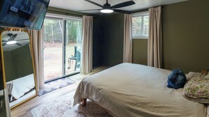 A bedroom with a bed, a ceiling fan, a TV, and a sliding glass door leading to an outdoor area. - Fabulous 3-bedroom cabin in welcoming Webb Lake perfect for relaxing (WEBB LAKE)