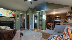 A living room with a fireplace, a television, a sofa, and a kitchen area in the background. - Fabulous 3-bedroom cabin in welcoming Webb Lake perfect for relaxing (WEBB LAKE)