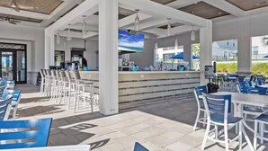 Un espace extérieur aménagé en terrasse, avec des sièges blancs et bleus, un comptoir de bar et un écran de télévision.