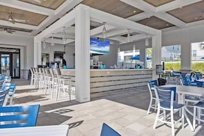An outdoor patio area with white and blue seating, a bar counter, and a television screen. - 9BR Luxury Disney Villa w/ Pool, Game Room & Resort Access (Four Corners)