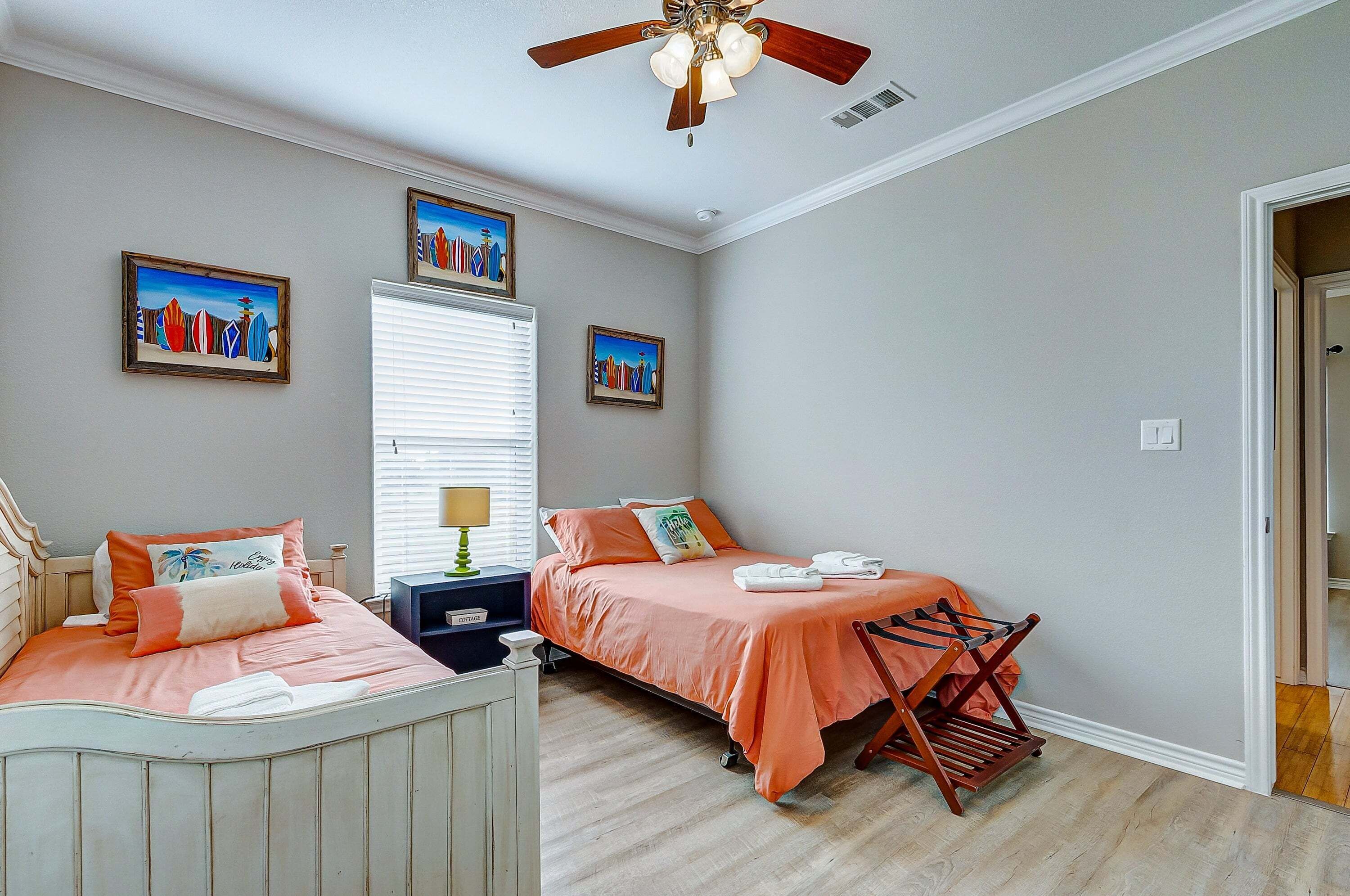 A bedroom with two beds, a ceiling fan, and artwork on the walls.