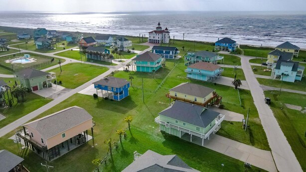 Vue aérienne d’une zone résidentielle côtière, avec des maisons, un phare et une plage.