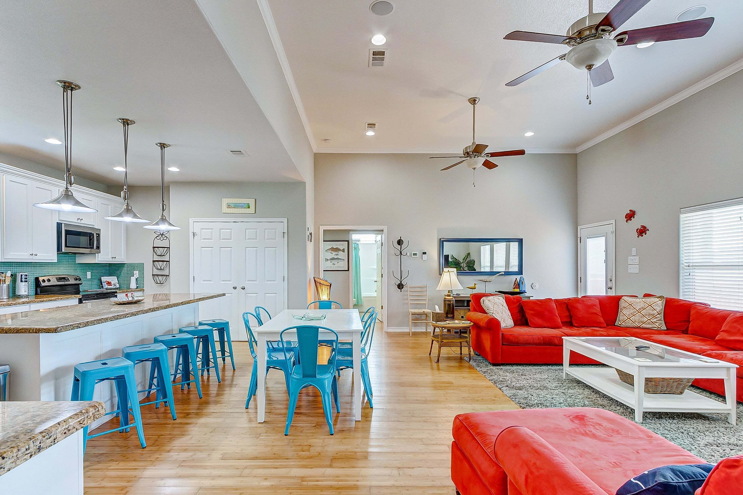 A spacious living area with a red sofa, a coffee table, and a dining area with blue chairs and a white table.
