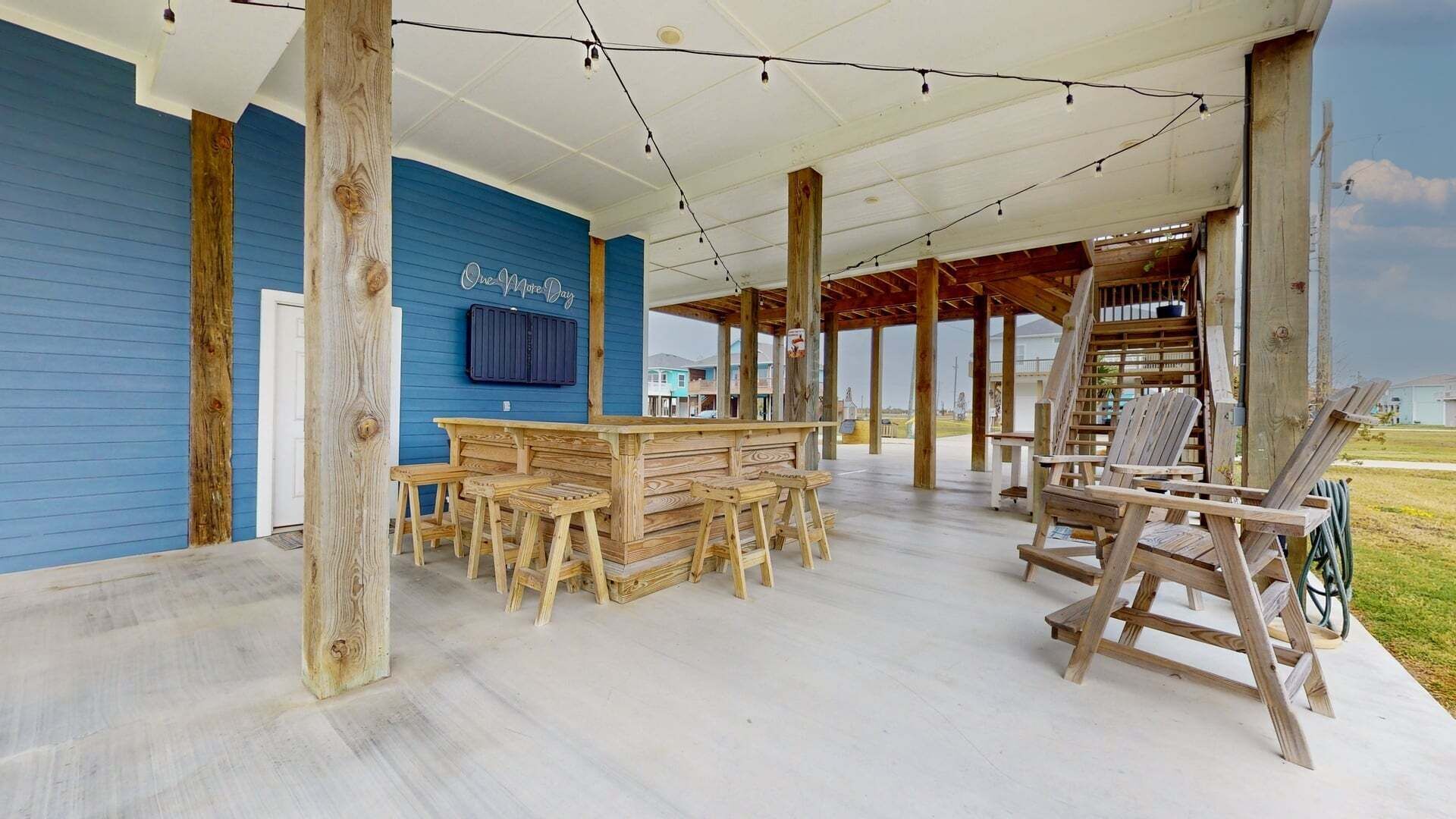 Un espace extérieur abrité, doté d’un bar en bois et de sièges, d’un mur bleu et offrant une vue sur les environs.
