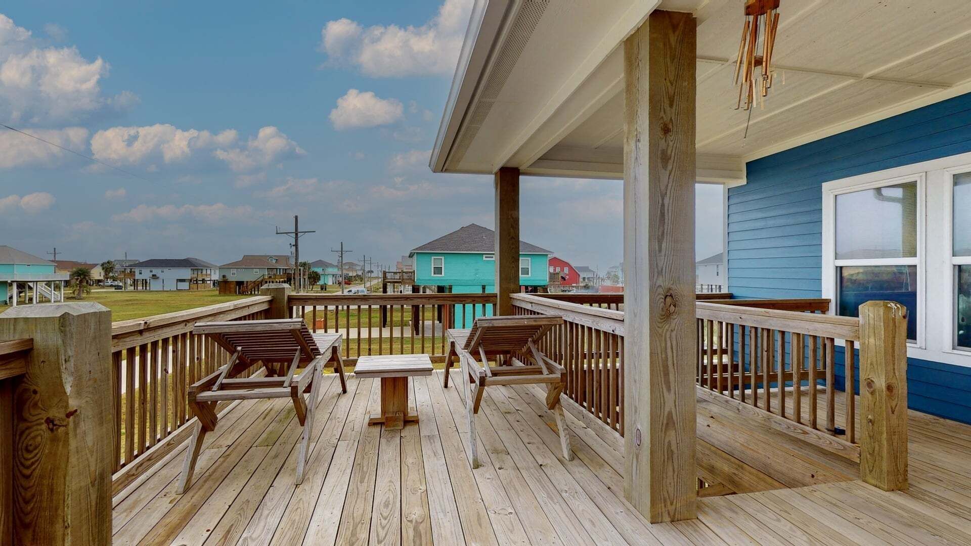 Une terrasse en bois avec une table et des chaises, un espace couvert avec une rambarde, et des maisons en arrière-plan.