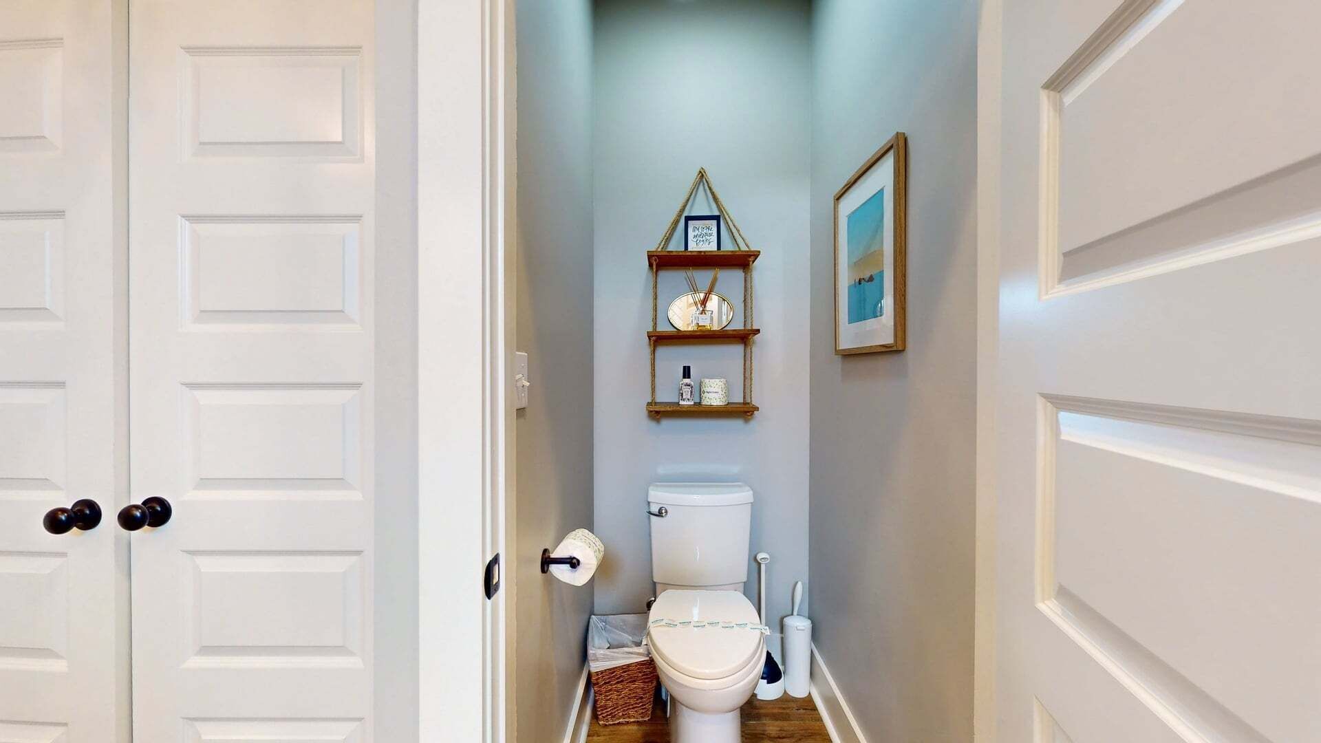 Ein schmaler Flur führt zu einem Badezimmer mit Toilette, Ablagen für Toilettenartikel und einem gerahmten Bild an der Wand.
