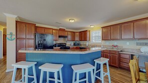 A kitchen with wooden cabinets, a refrigerator, a microwave, and a coffee station. - Lime In The Coconut 3 Bedroom Home (Port Bolivar)