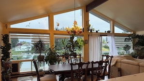 A dining area with a table and chairs, large windows, and various potted plants. - The Green Heaven at the Lake (Lake Tapps)