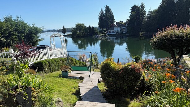 A wooden pathway leading to a white fence, surrounded by greenery and a lake view. - The Green Heaven at the Lake (Lake Tapps)