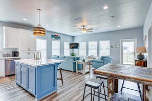 A modern kitchen with a blue island, white cabinets, and a ceiling fan. - Afterdunedelight 3 Bedroom Home (Port Bolivar)