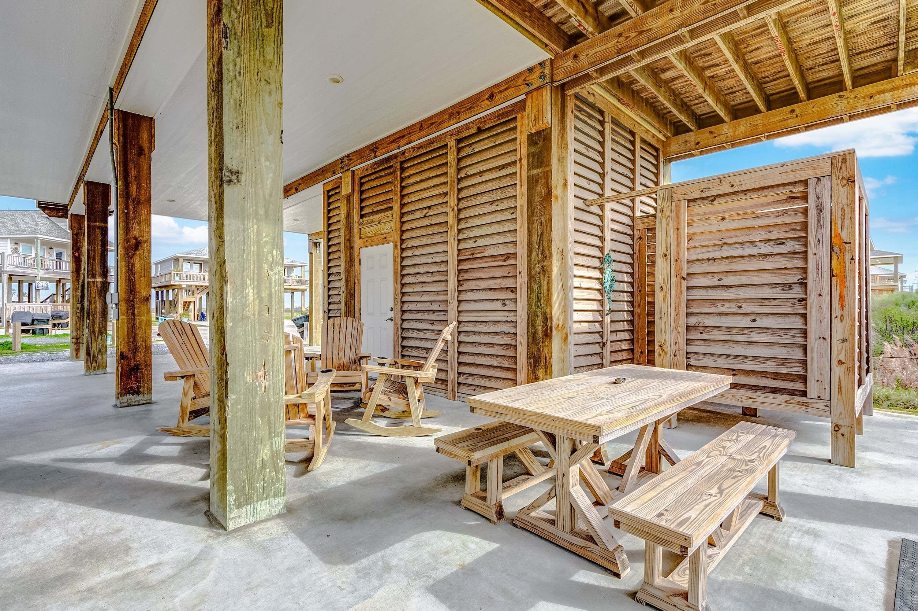 An outdoor wooden deck with a picnic table and benches, surrounded by wooden walls and columns.