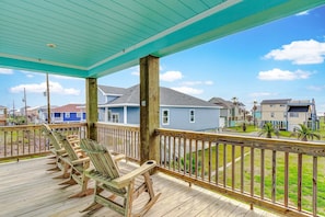 A covered porch with wooden chairs, a view of houses, and a clear sky. - Afterdunedelight 3 Bedroom Home (Port Bolivar)