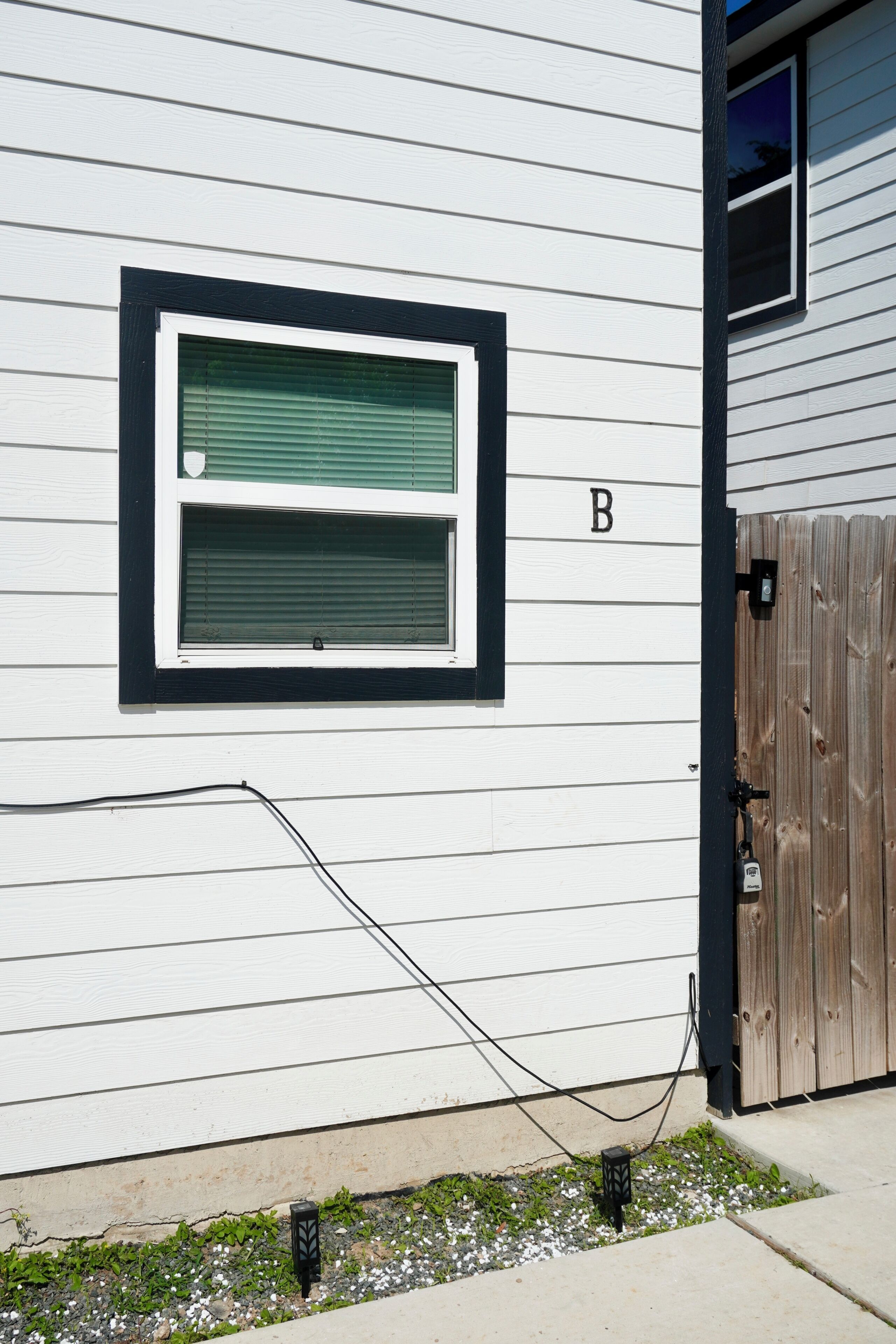 A white building with a window, a wooden fence, and a small patch of grass.