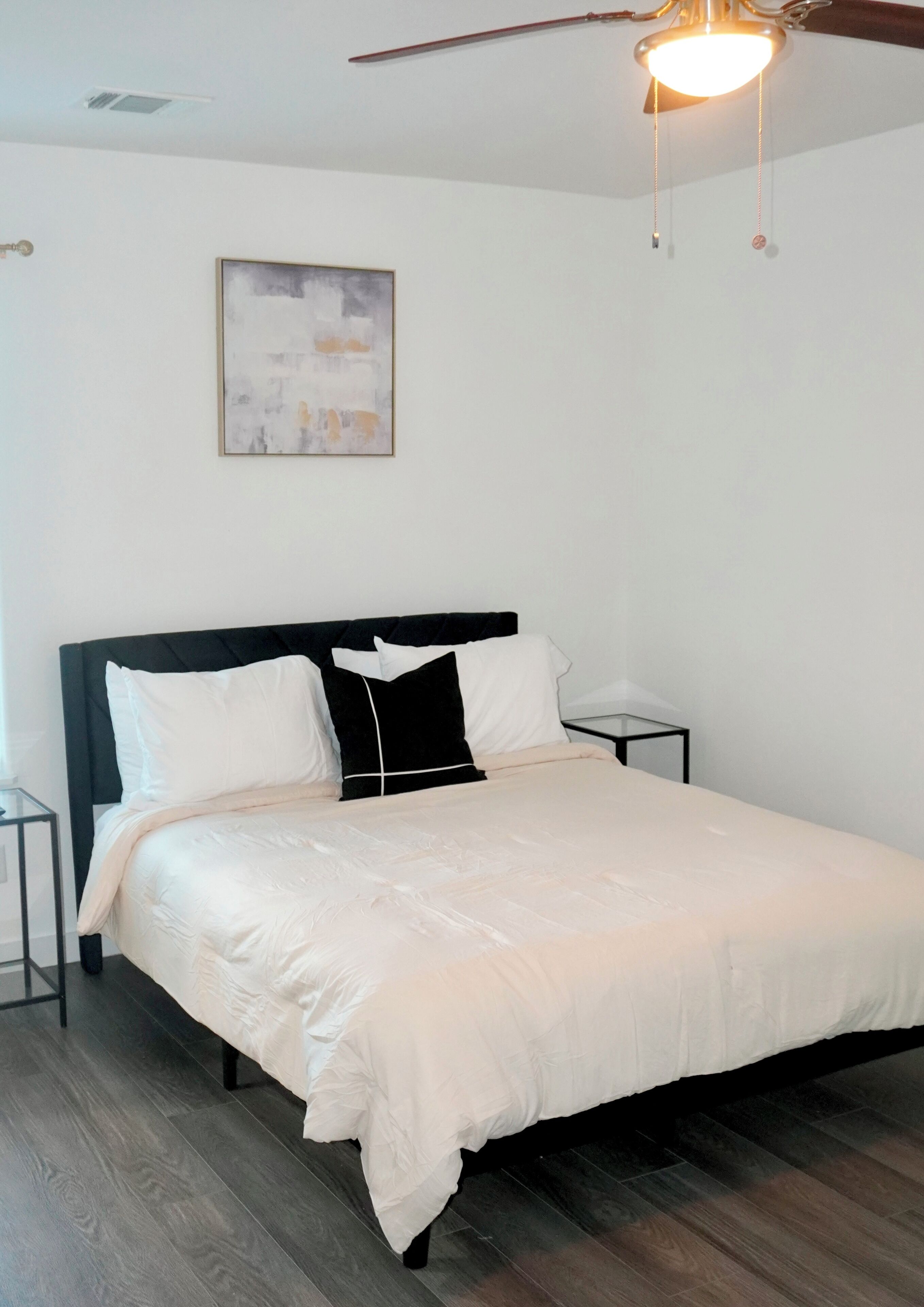 A bedroom with a bed, a nightstand, a ceiling fan, and a wall-mounted light fixture.