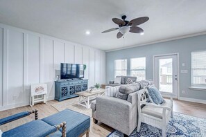 A living room with a TV, blue cabinet, grey sofa, and a ceiling fan. - Oceanview 4 Bedroom Home (Port Bolivar)