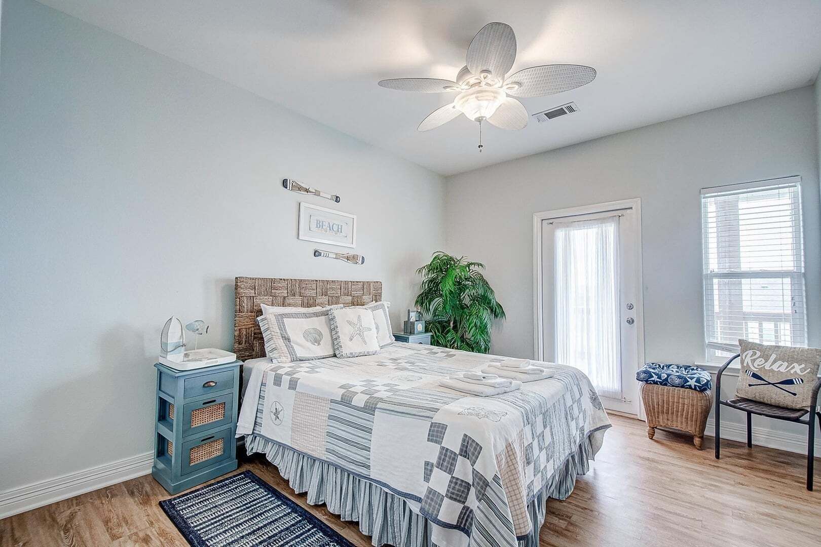 A bedroom with a bed, a nightstand, a chair, a ceiling fan, a door, and a window.