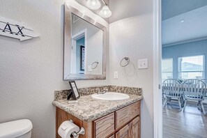 A bathroom with a white sink, wooden vanity, a mirror, and a toilet. - Oceanview 4 Bedroom Home (Port Bolivar)