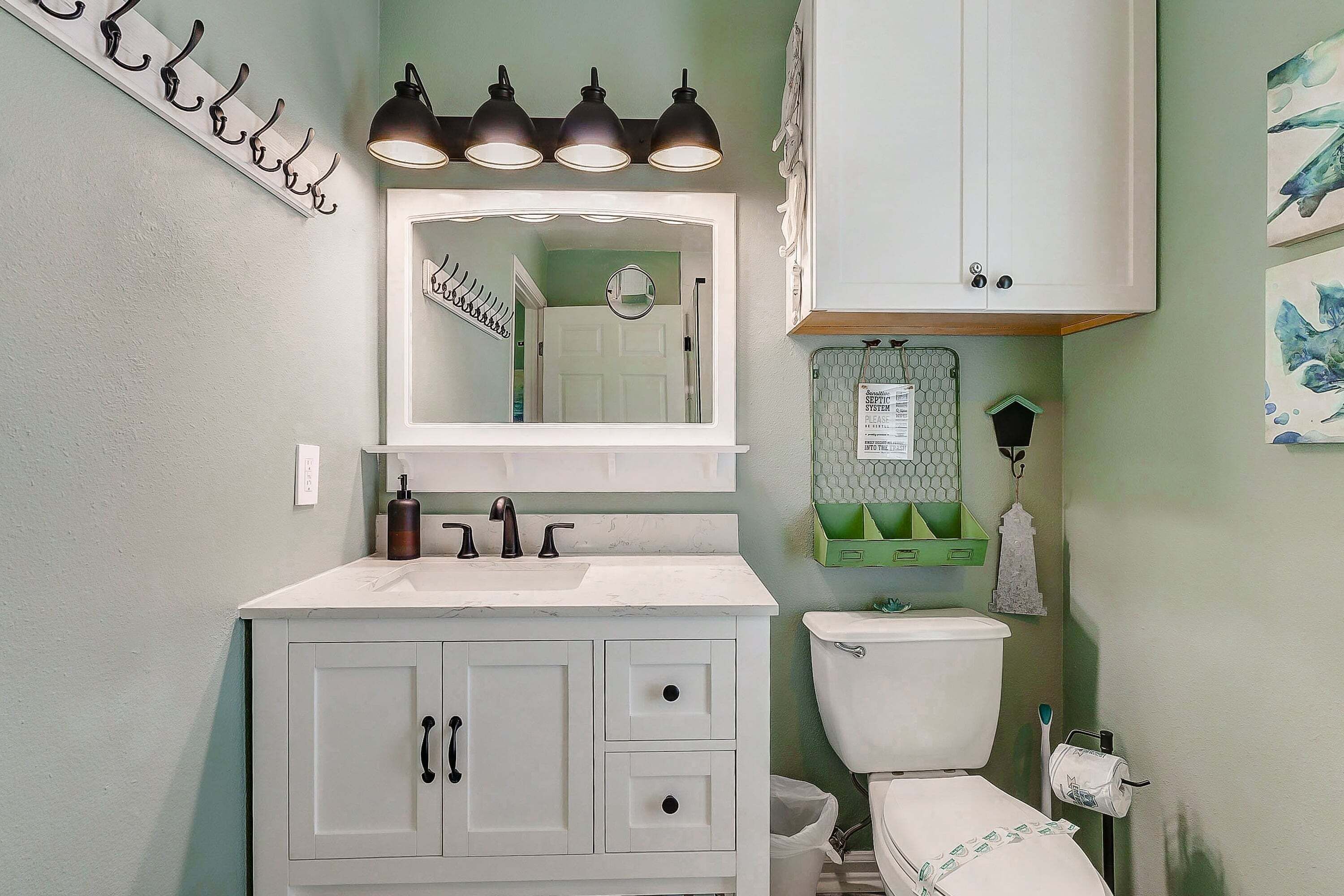 Un baño con tocador blanco, un espejo, inodoro y pared verde.