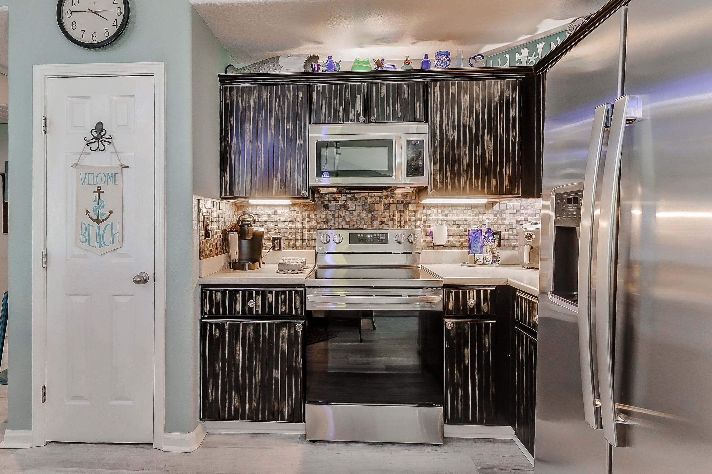 Una cocina con gabinetes oscuros, un refrigerador de acero inoxidable, un microondas y un horno.