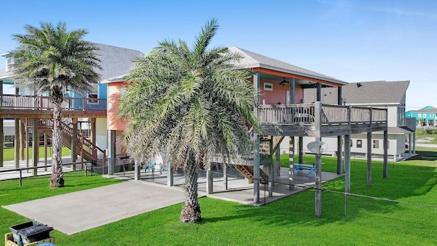 Ein Strandgrundstück mit Holzterrasse, Palmen und einem Gebäude mit Balkon.