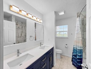 Ein Badezimmer mit Waschbecken, Spiegel, Handtuchhalter, Toilette und Duschvorhang.