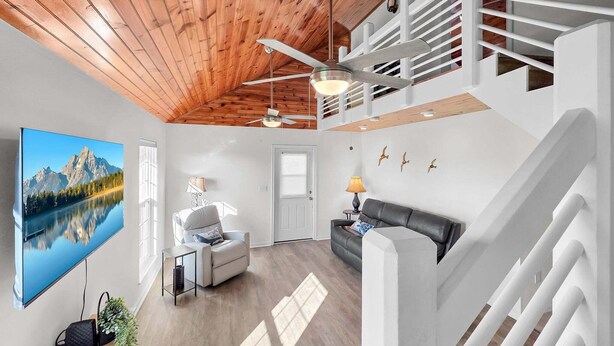 A spacious living area with a wooden ceiling, a large TV, a sofa, and a staircase. - Over The Rainbow 3 Bedroom Home (Port Bolivar)