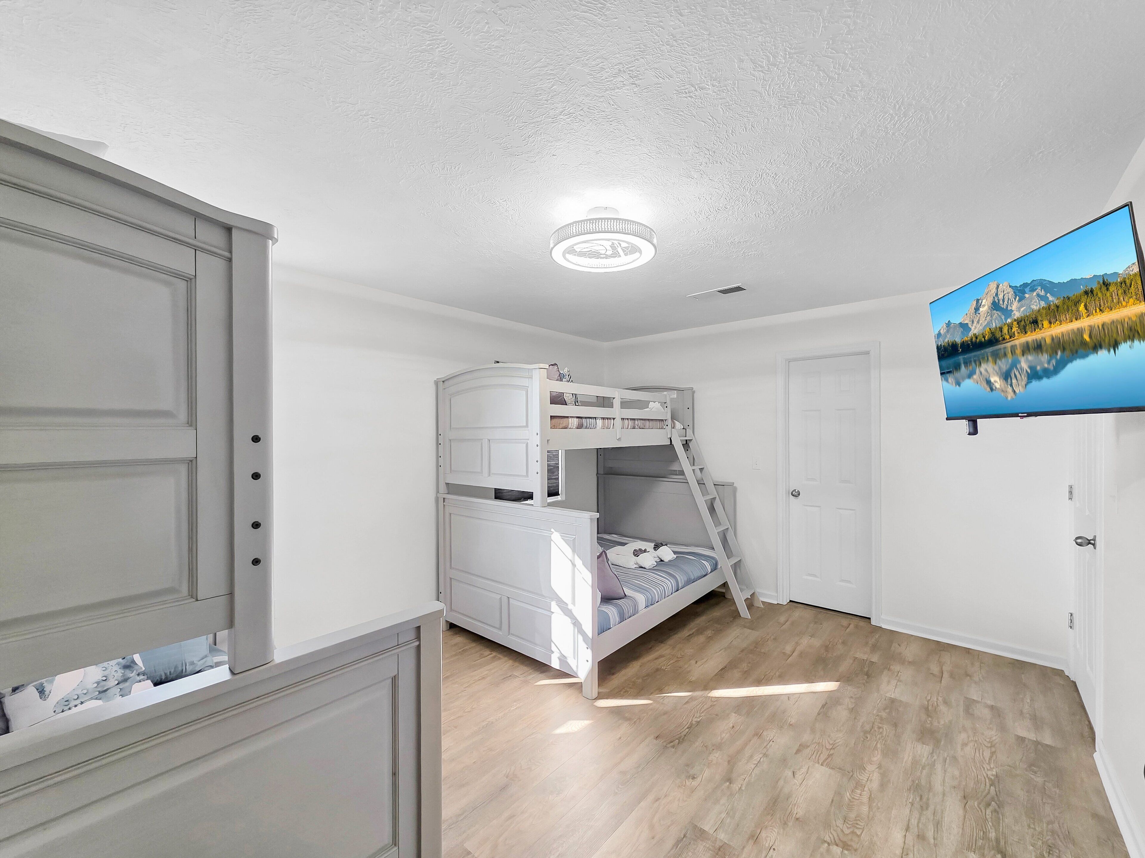 A room with a bunk bed, a television mounted on the wall, and a door with a handle.