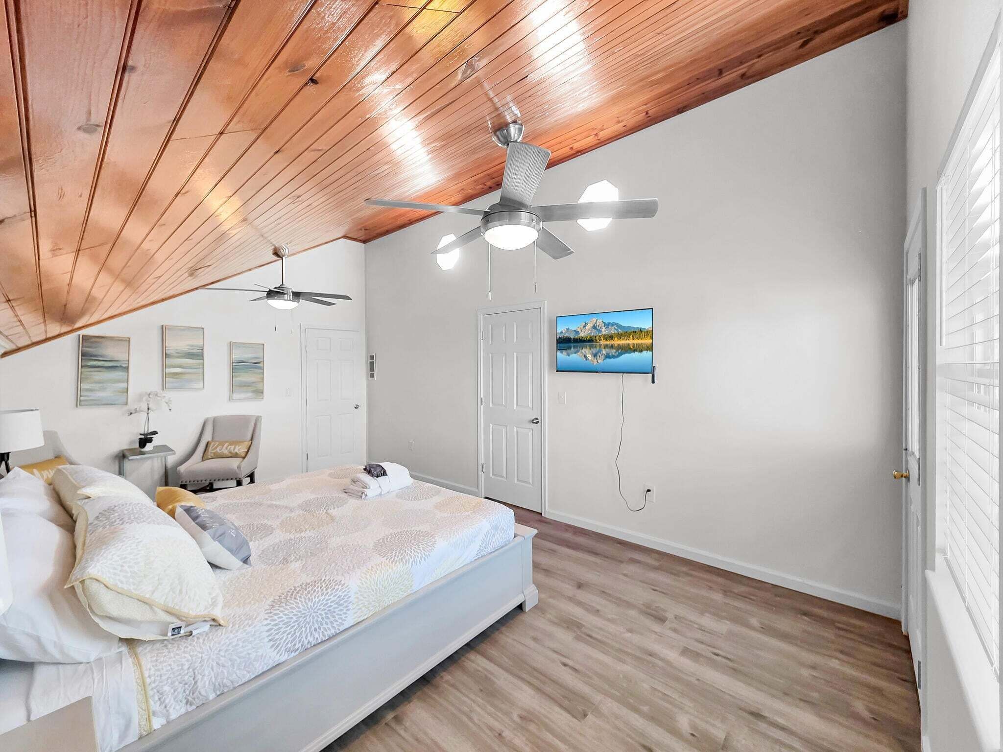Une chambre à coucher avec un lit, deux ventilateurs de plafond, un téléviseur fixé au mur et une porte.