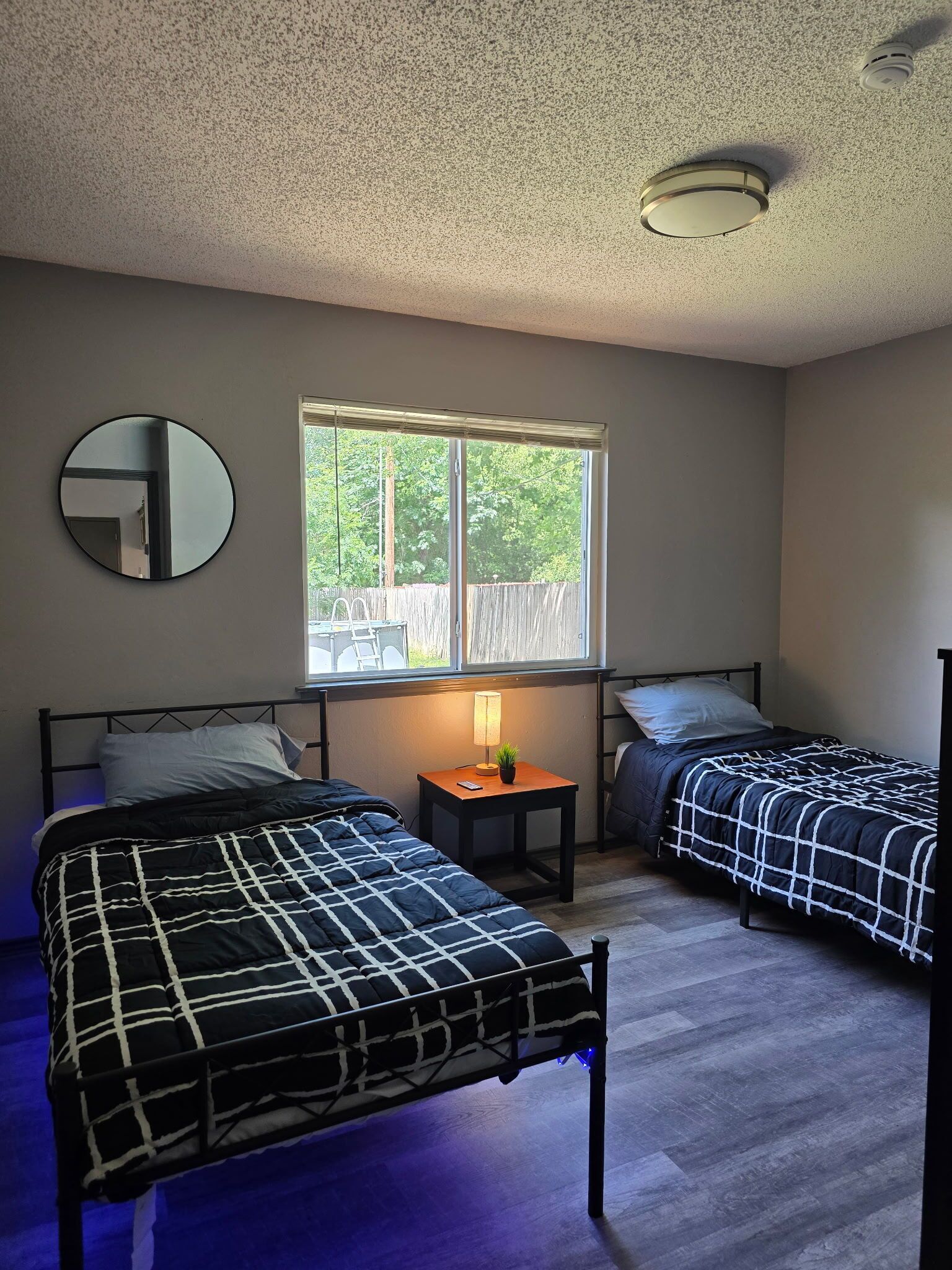 A bedroom with two beds, a window, a mirror, and a ceiling light.