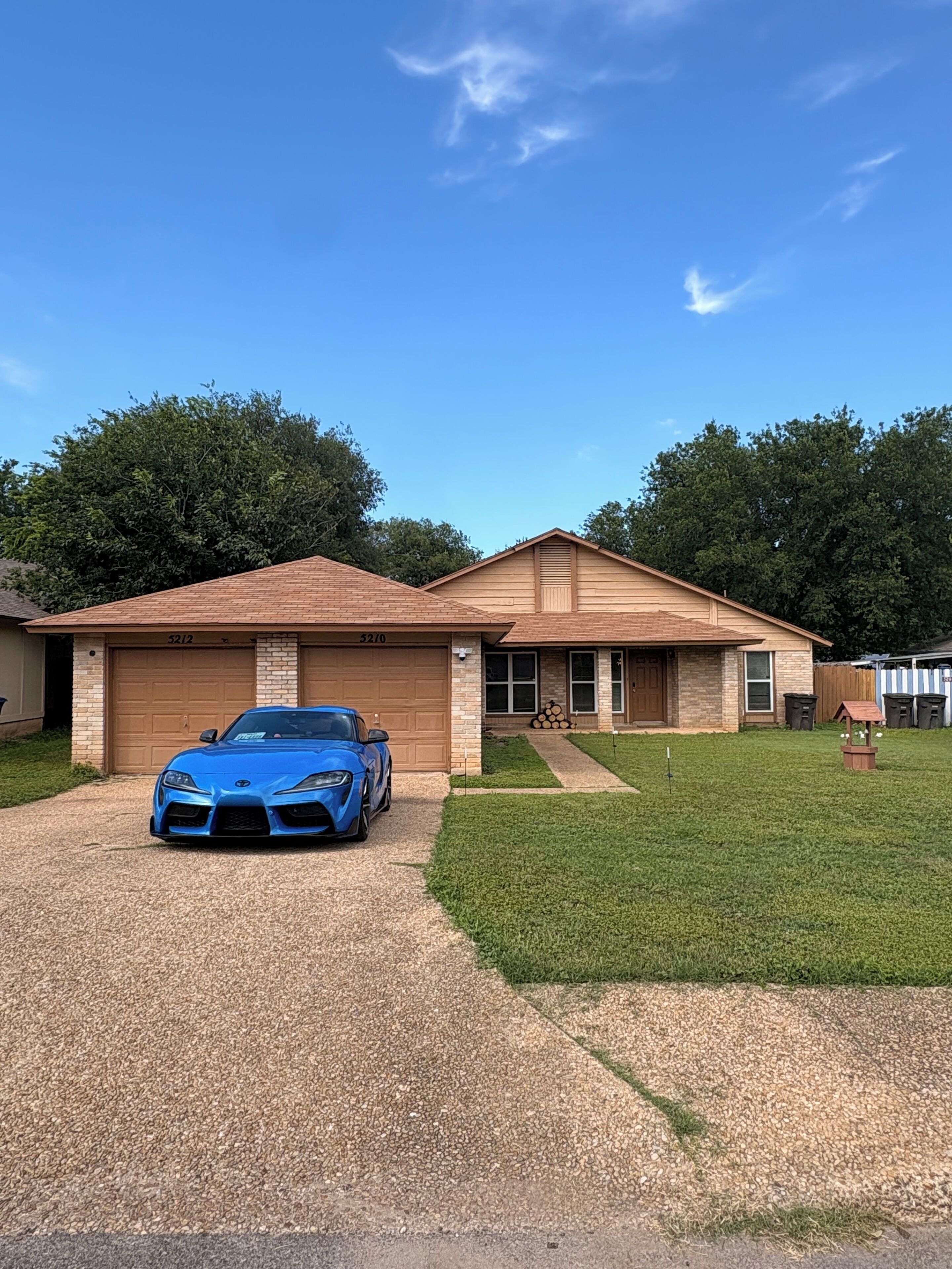 Uma casa de dois andares com garagem, entrada para carros e um carro esportivo azul estacionado na frente.