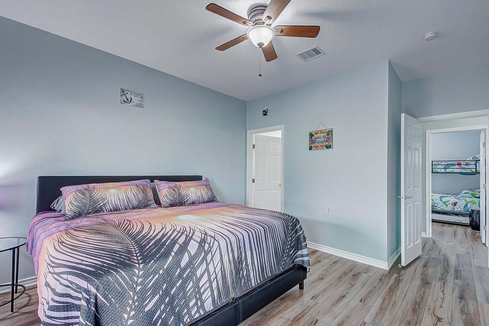 Un dormitorio con una cama, ventilador de techo, una puerta y un pasillo que conduce a una litera.