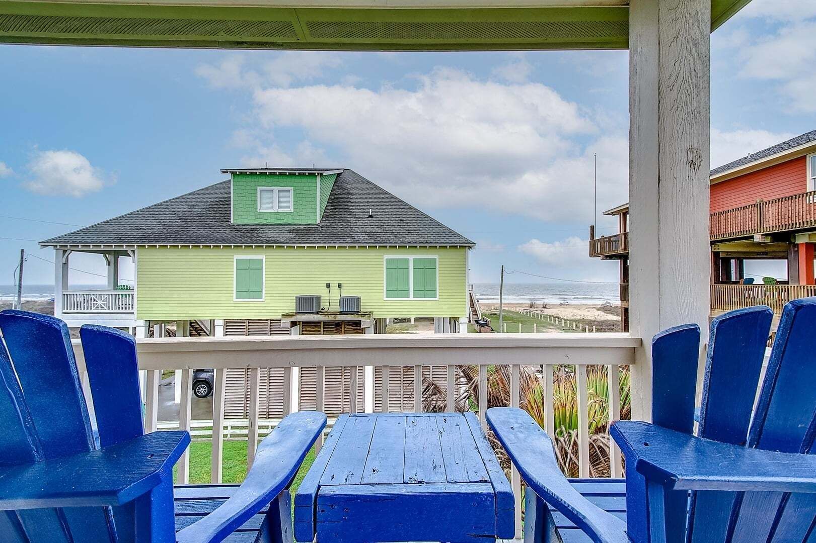 Una casa verde con balcón, sillas azules y vista al océano.