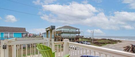 A balcony with a view of the ocean, a beach, and a building with a balcony.