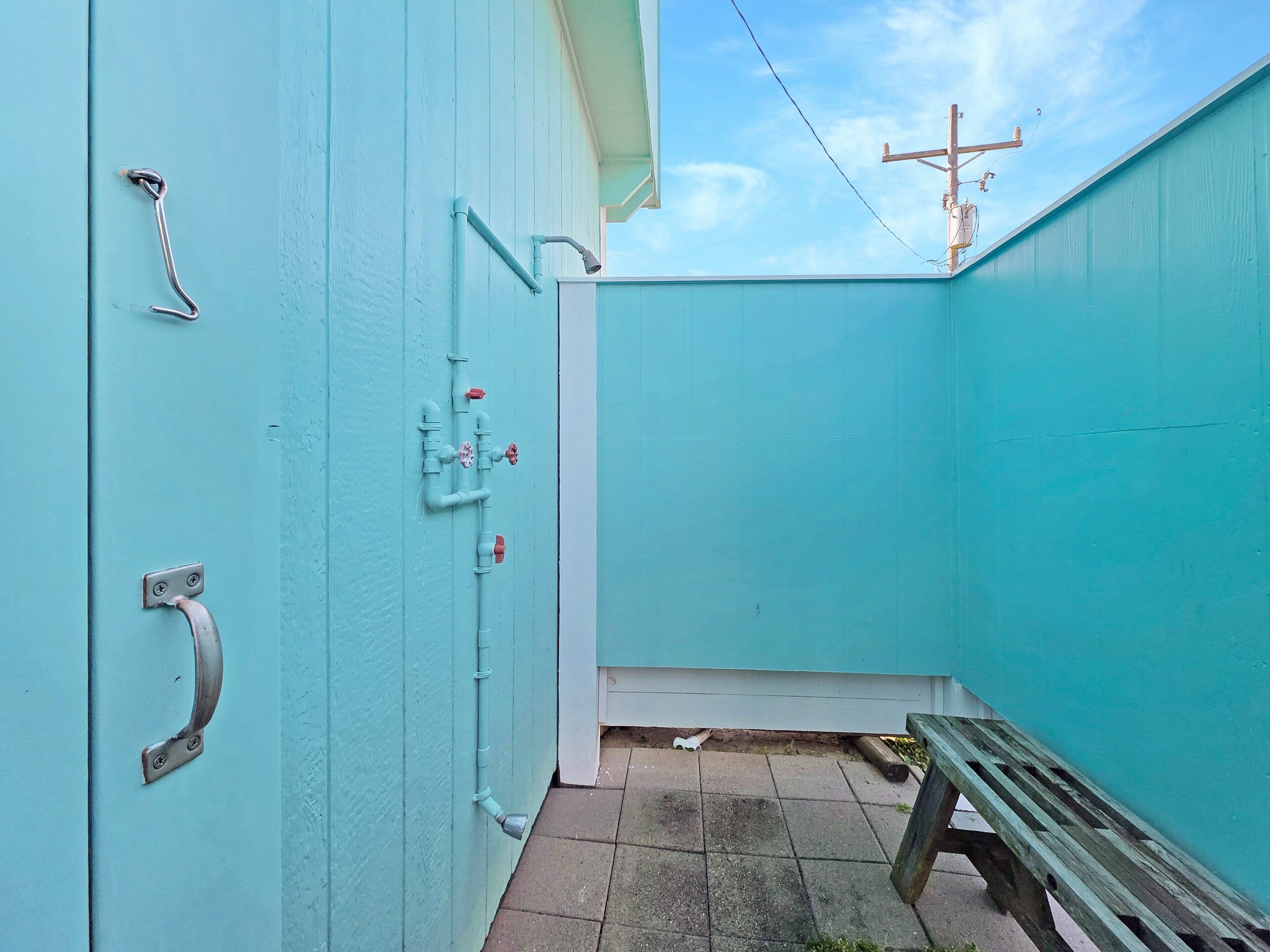 A narrow outdoor area with a bench, a metal gate, and a utility box with pipes and valves.