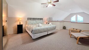 Une chambre à coucher comprenant un lit, deux tables de chevet, un ventilateur de plafond, une fenêtre et une petite table avec une chaise.