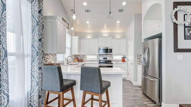 A modern kitchen with white cabinetry, a central island with bar stools, stainless steel appliances, and pendant lighting. - Casa Chillax 4 Bedroom Home (Port Bolivar)
