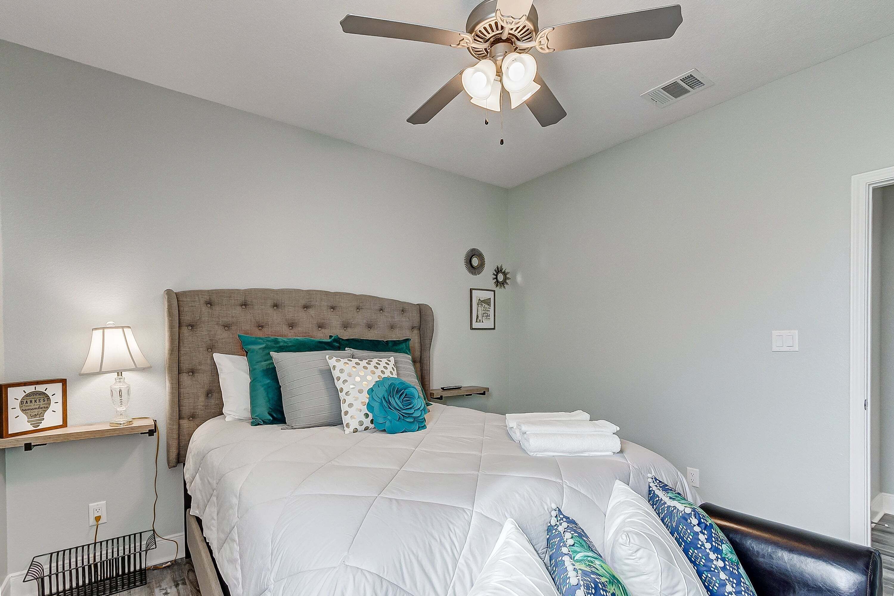 A bedroom with a bed, a ceiling fan, a bedside table with a lamp, and a wall clock.