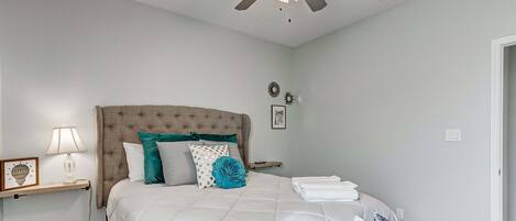A bedroom with a bed, a ceiling fan, a bedside table with a lamp, and a wall clock.