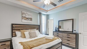 A bedroom with a bed, a ceiling fan, a nightstand, a dresser, a mirror, and a door. - Casa Chillax 4 Bedroom Home (Port Bolivar)